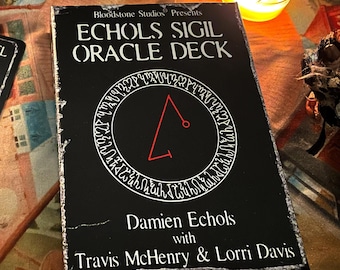 May include: Two black oracle cards with red sigils and white text. The card on the left reads "Archangel Asmodel, Archangel of Taurus, Physical Health, Financial Success, Success in Business". The card on the right reads "Bloodstone Studios Presents, Echols Sigil Oracle Deck, Damien Echols with Travis McHenry & Lorri Davis".