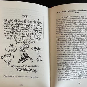 May include: An open book with white pages showing black text and illustrations. The left page features a handwritten document with symbols and the caption 'Pact signed by the demons with their promises.' The right page contains text titled 'Christoph Haizmann &ndash; Possessed through a Pact' and the page number 159.