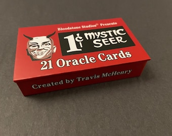 May include: A rectangular red box for 21 Oracle Cards titled 1¢ Mystic Seer. The box features a white illustration of a horned face on the left, a black rectangular logo with white text, and the creator name Travis McHenry printed in white.