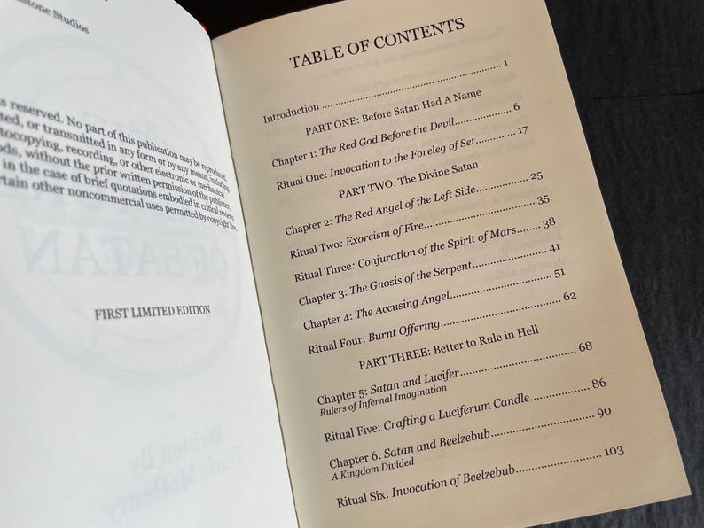 May include: An open book displaying a Table of Contents page with black text on a cream-colored background. The text lists sections including Part One: Before Satan Had A Name, Part Two: The Divine Satan, and Part Three: Better to Rule in Hell.