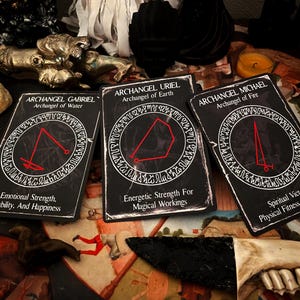 May include: Three black tarot cards with red and white text. The cards are titled "Archangel Gabriel, Archangel of Water", "Archangel Uriel, Archangel of Earth", and "Archangel Michael, Archangel of Fire". Each card has a red symbol in a circle.