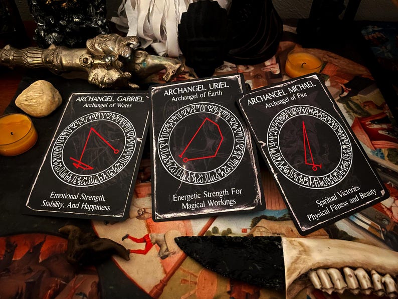May include: Three black tarot cards with red and white text. The cards are titled "Archangel Gabriel, Archangel of Water", "Archangel Uriel, Archangel of Earth", and "Archangel Michael, Archangel of Fire". Each card has a red symbol in a circle.