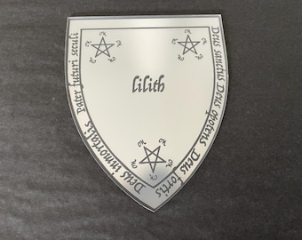 May include: A shield-shaped, silver-colored emblem with the name "Lilith" in the center. The emblem features three pentagrams and text in a circular pattern around the edge. The background is a dark gray.