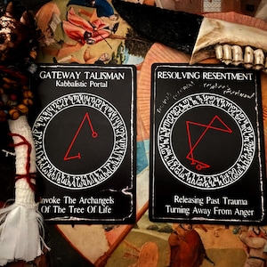 May include: Two black cards with white text and red symbols. The card on the left says "Gateway Talisman Kabbalistic Portal" and the card on the right says "Resolving Resentment".
