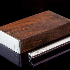 Puede incluir: Una caja de madera con una tapa de metal plateado y una pipa de metal plateado con la palabra "Whiff" grabada.