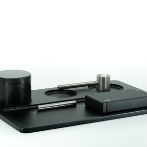 May include: A black rolling tray with a grinder, a small metal pipe, a metal poker, and a black box with a textured lid.