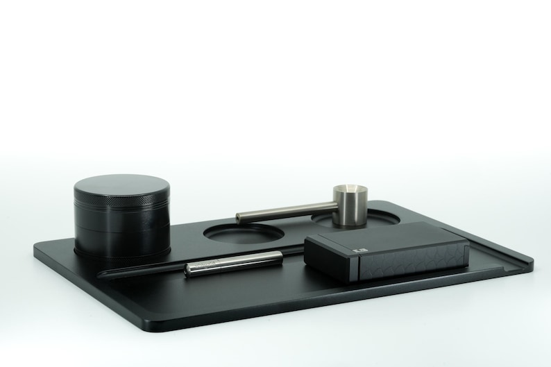 May include: A black rolling tray with a grinder, a small metal pipe, a metal poker, and a black box with a textured lid.