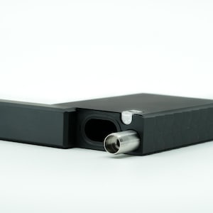 May include: A black rectangular box with a hinged lid, open to reveal a silver metal mouthpiece. The box has a textured surface and a small silver latch.