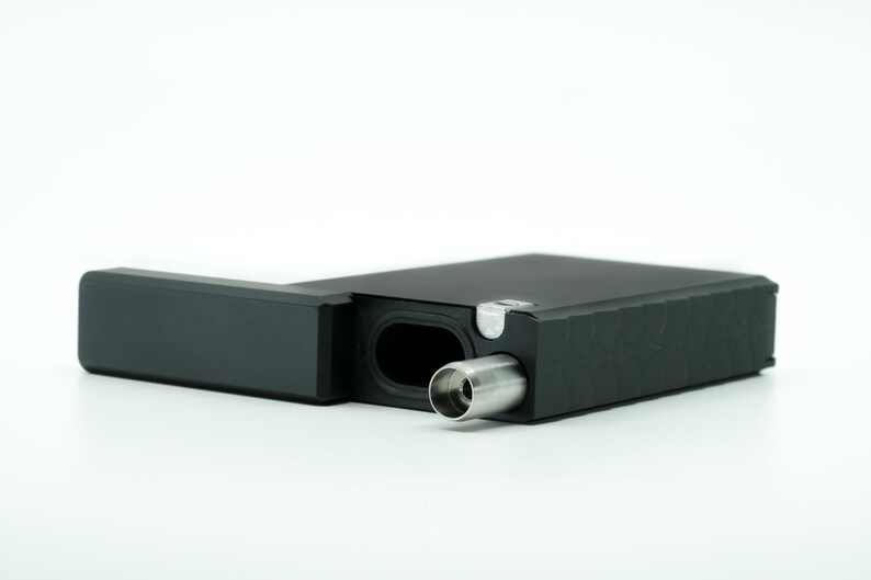 May include: A black rectangular box with a hinged lid, open to reveal a silver metal mouthpiece. The box has a textured surface and a small silver latch.