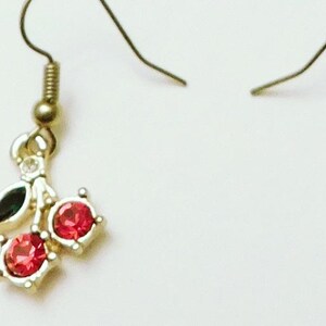 May include: Gold dangle earrings with red and green crystal cherries.