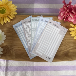 Könnte beinhalten: Ein Set aus fünf rechteckigen Spar-Challenge-Karten aus Papier, die fächerförmig angeordnet sind. Jede Karte ist mit 1€, 2€, 5€, 10€ oder 20€ Challenge beschriftet und enthält ein Raster aus kleinen Kästchen sowie eine 100€-Gesamtsumme.