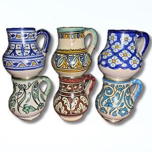 May include: Six small ceramic pitchers with hand-painted designs in various colours. The pitchers have curved handles and are decorated with blue, white, red, and green patterns. They are stacked in pairs, highlighting their decorative appeal.