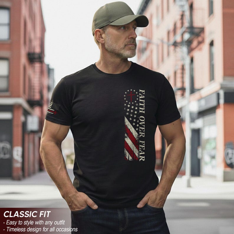 May include: Black t-shirt featuring a distressed American flag design with the text "FAITH OVER FEAR." The shirt has a classic fit and is paired with blue jeans and a green cap. The sleeve has a small American flag design.