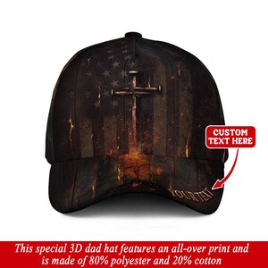 Może przedstawiać: Czarna czapka typu dad hat z nadrukiem przedstawiającym amerykańską flagę i krzyż. Czapka ma napis "YOURTEXT" na rondzie i "CUSTOM TEXT HERE" na czerwonej etykiecie. Wykonana w 80% z poliestru i 20% z bawełny.
