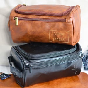 May include: Two leather travel toiletry bags. The top bag is brown with the name "Victor JAMES" in gold lettering. The bottom bag is black with the initials "G P" in gold lettering.