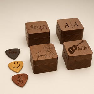 May include: A collection of personalized wooden boxes and guitar picks. The boxes are square with engraved designs, including names, initials, a guitar, and a heartbeat. The guitar picks have various designs, including a smiley face and a peace sign.