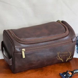 May include: A brown leather travel toiletry bag with a zipper closure and a gold zipper pull. The bag has a handle and the text "Charlie ROBERT" is printed on the front.