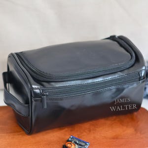 May include: Black leather travel toiletry bag with a zipper closure and a handle. The bag has the name "JAMES WALTER" embossed on the front.