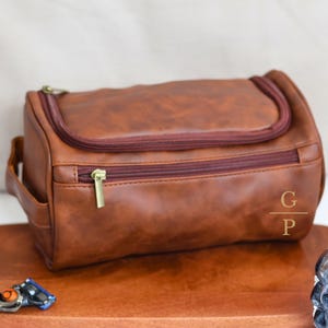 May include: A brown leather travel bag with a zipper closure and a gold zipper pull. The bag has a monogrammed "G/P" on the side.