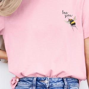 May include: A pink t-shirt with a bee graphic and the text "bee you" printed on the front.