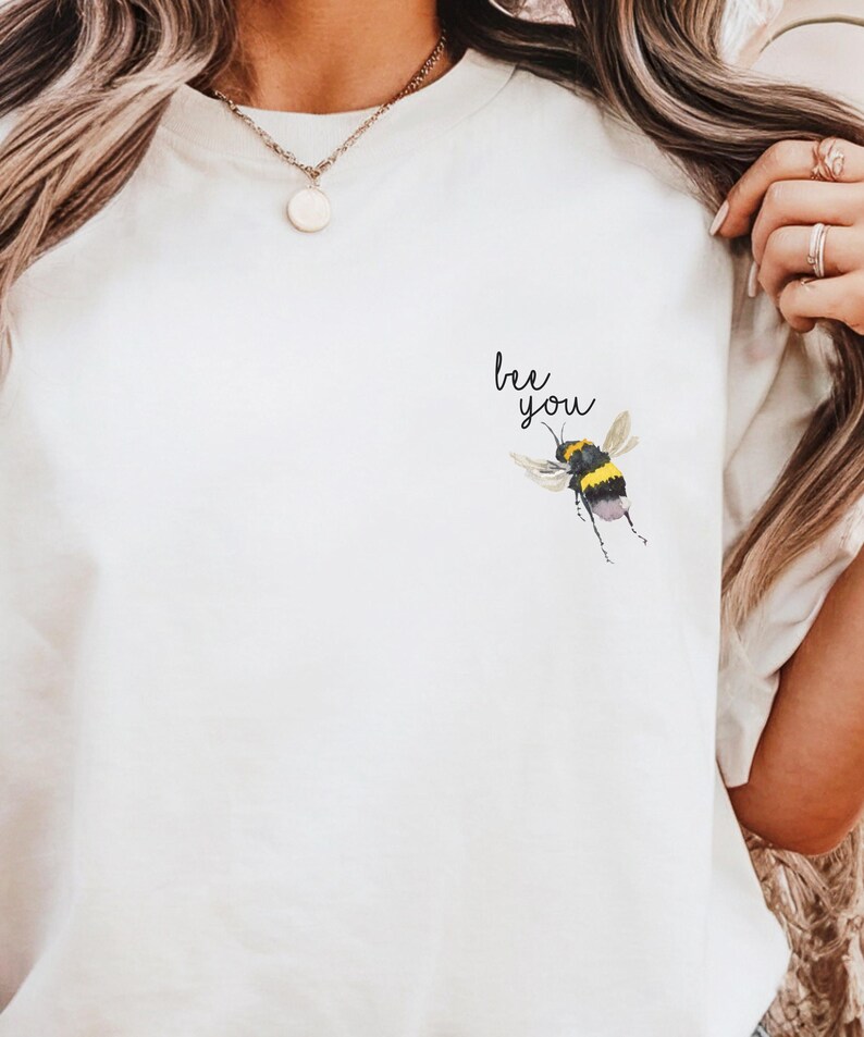 May include: White t-shirt with a bee graphic and the text "bee you" printed on the front.