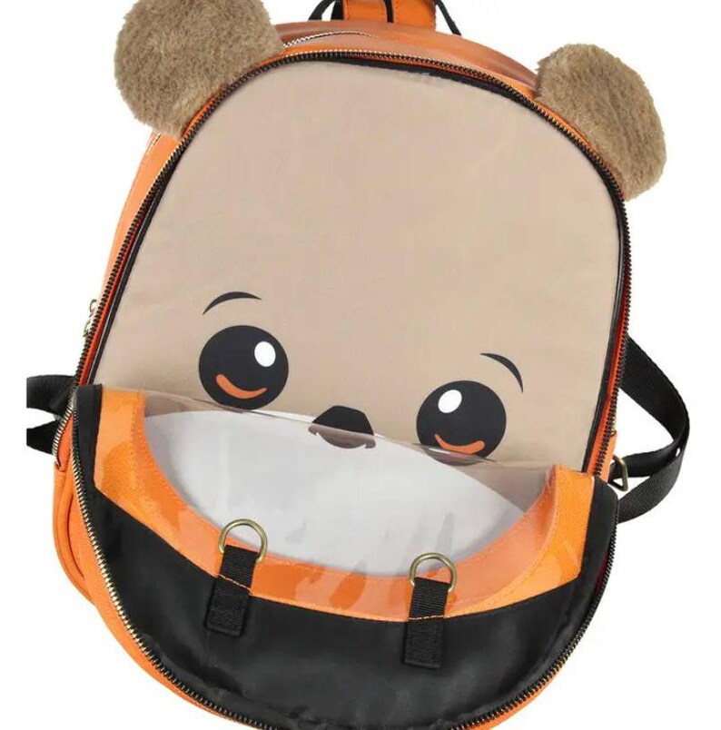 Puede incluir: Mochila naranja y negra con un dise&ntilde;o de cara de oso de dibujos animados. La mochila presenta un bolsillo frontal grande y transparente, orejas marrones y difusas y correas negras. La cremallera es negra y la mochila tiene herrajes met&aacute;licos dorados.
