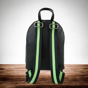 Puede incluir: Mochila negra con correas para los hombros a rayas verdes brillantes y negras. La mochila tiene un asa superior y hebillas de metal plateado. La bolsa est&aacute; hecha de un material texturizado.