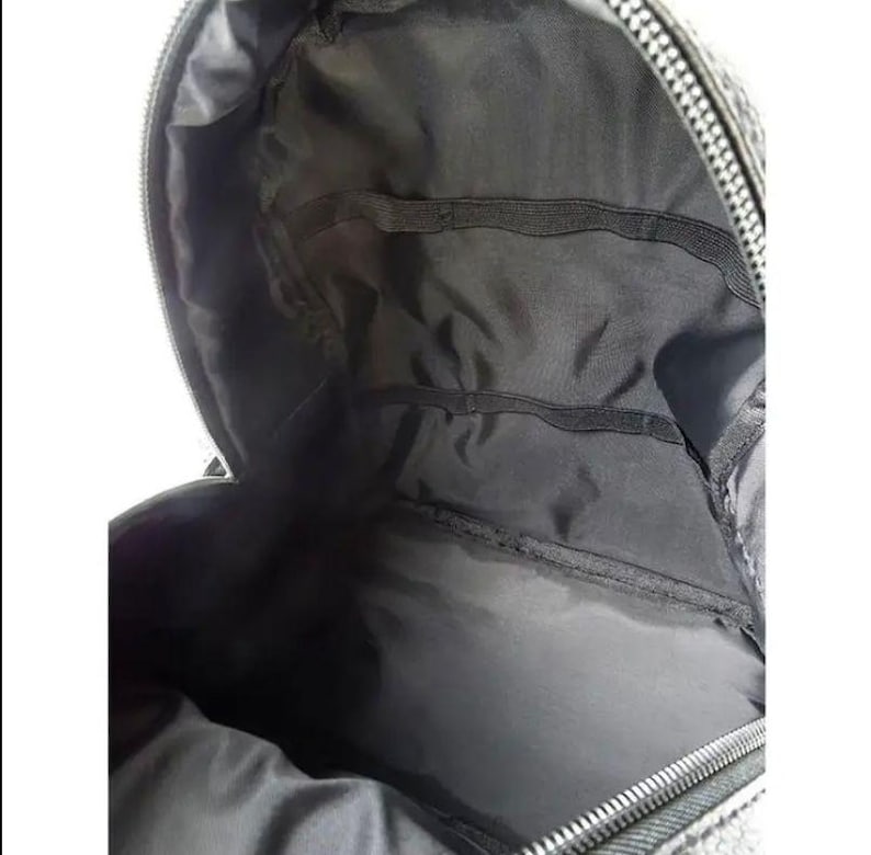 Puede incluir: Vista interior de una mochila negra. El interior cuenta con m&uacute;ltiples compartimentos y bolsillos, con cierre de cremallera. El forro es de tela gris oscuro. La mochila est&aacute; dise&ntilde;ada para transportar objetos.