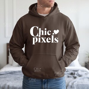 Może przedstawiać: Brązowa bluza z kapturem z białym nadrukiem, na którym widnieje napis "Chic. pixels" z białym symbolem serca.