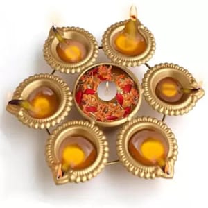 May include: A golden, star-shaped candle holder with six oil lamps surrounding a central bowl. The lamps are filled with oil and have lit wicks, and the central bowl holds a lit candle and flower petals. The arrangement is on a white background.