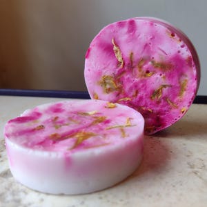 Könnte beinhalten: Zwei runde rosa und weiße Seifenstücke mit getrockneten Blütenblättern, die in die Seife eingebettet sind.
