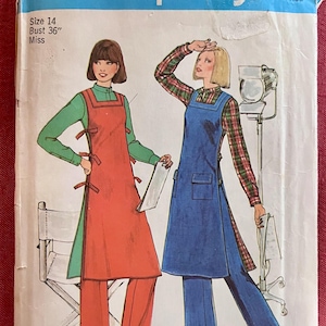 May include: A Simplicity sewing pattern envelope, number 7426, for a size 14, 36-inch bust garment. The illustration shows two variations of a sleeveless apron-style tunic worn over long-sleeved shirts and trousers, with side tie closures.
