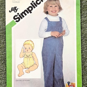 Könnte beinhalten: Simplicity Schnittmuster 5255 für eine Baby-Latzhose. Das Cover zeigt ein lächelndes Kind in einer blauen Latzhose über einem weißen Rollkragenpullover. Das Muster enthält zwei Größen, 1/2 und 1. Der Text "Embroidery not included" ist sichtbar.