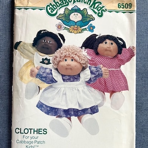 May include: A Butterick sewing pattern envelope for Cabbage Patch Kids clothes, number 6509. The front features three dolls wearing different outfits: a yellow dress with a white apron, a pink polka dot dress, and a blue floral dress with a white apron.