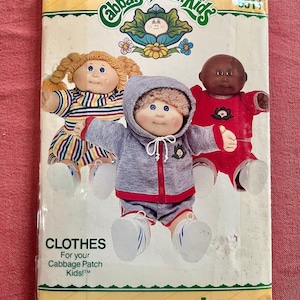 Op de afbeelding: Een Butterick naaipatroon-envelop voor Cabbage Patch Kids-kleding met illustraties van drie poppen. Eén pop draagt een gestreepte jurk, één een grijs joggingpak met capuchon en één een rode outfit. De tekst luidt Cabbage Patch Kids en Butterick.