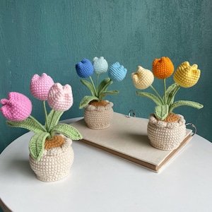 May include: Three crocheted flower arrangements in pots. The first arrangement has pink tulips, the second has blue and light blue tulips, and the third has yellow, orange, and light yellow tulips.