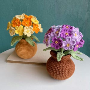 May include: Two crocheted flower arrangements in brown pots. One arrangement has yellow and orange flowers, the other has purple flowers.