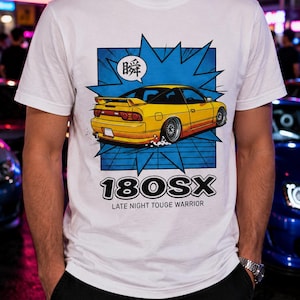 Könnte beinhalten: Ein weißes T-Shirt mit einer Grafik eines gelben 180SX Sportwagens auf blauem Hintergrund im Comic-Stil. Das Design enthält das japanische Schriftzeichen 瞬 in einer Sprechblase, den Text 180SX und die darunter gedruckten Worte LATE NIGHT TOUGE WARRIOR.
