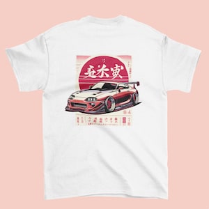 Puede incluir: Camiseta blanca con una ilustración roja y blanca de un coche deportivo con alerón. El gráfico incluye texto japonés y un diseño de sol rojo en el fondo. El coche es rojo y blanco.