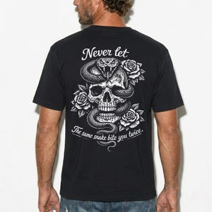 Peut inclure: Un t-shirt noir à manches courtes avec un motif blanc au dos. Le dessin représente un crâne entrelacé d'un serpent et entouré de roses. Le texte indique "Never let the same snake bite you twice.." dans une police blanche stylisée.