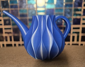 Könnte beinhalten: Eine leuchtend blaue Gießkanne mit einem einzigartigen, strukturierten Design. Sie hat einen langen Ausguss und einen gebogenen Griff, ideal für den Garten. Das Design ist modern und dekorativ, etwa 25 cm lang.