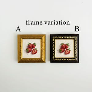 May include: Two framed strawberry art prints. One frame is gold, the other is black. Each print features a still life of ripe strawberries on a white background. The text "frame variation" is above the frames, with "A" and "B" to the left and right.