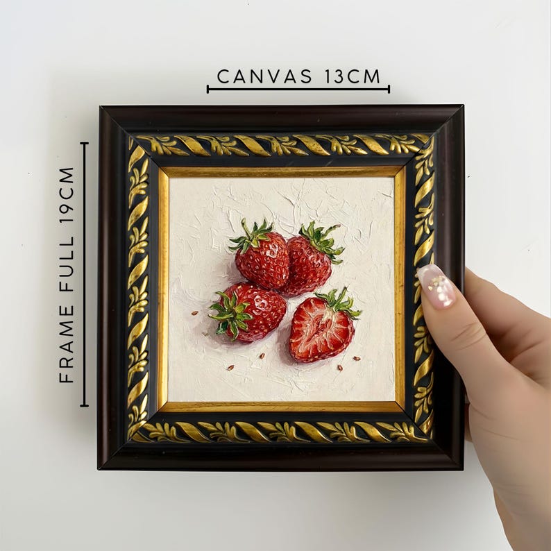 May include: A framed painting of strawberries. The canvas measures 13cm, and the full frame is 19cm. The painting features four red strawberries with green leaves on a white background. The frame is dark brown with gold accents.