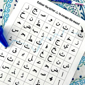 May include: A white paper maze game with Arabic letters, a blue marker, and an orange marker. The text "Colour the letter to escape the maze!" is printed at the top. A blue line traces a path through the maze.
