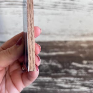 Puede incluir: Primer plano del lateral de una posavasos de madera. La posavasos est&aacute; hecha de madera marr&oacute;n claro con un acabado liso. La posavasos est&aacute; siendo sostenida por una mano.