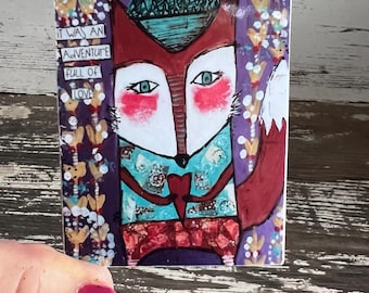 May include: A whimsical illustration of a fox wearing a blue and green hat and a red scarf. The fox has a white face with blue eyes and red cheeks. The background is purple with white flowers. The text "It was an adventure full of love" is written in black on white rectangles.