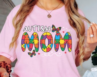May include: Pink t-shirt with the text "Autism Mom" in colorful puzzle pieces and butterflies.