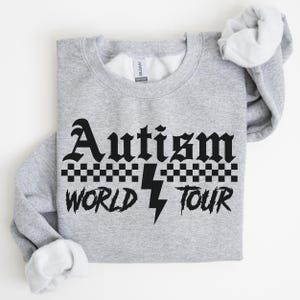 May include: A gray sweatshirt with black text that reads "Autism World Tour" with a lightning bolt and checkered pattern.