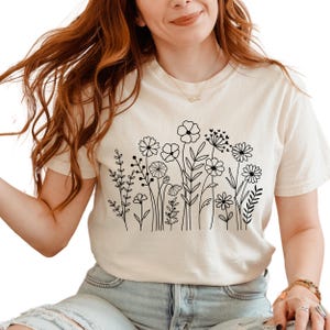 May include: A white t-shirt with a black line drawing of a field of flowers.