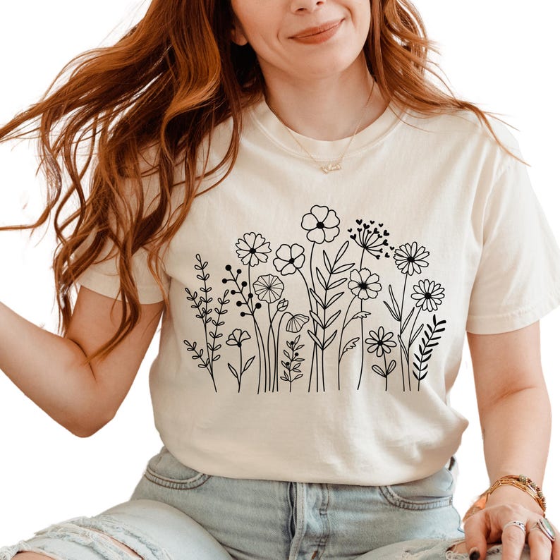 May include: A white t-shirt with a black line drawing of a field of flowers.